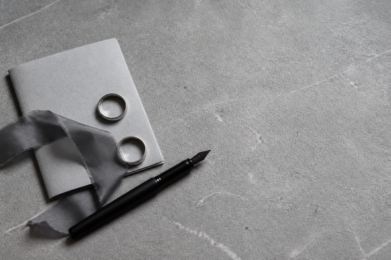 Dos anillos, una tarjeta y una pluma sobre una superficie de piedra gris