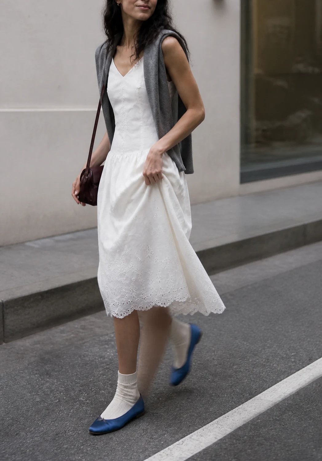Mujer joven caminando con un vestido blanco bordado y pequeños detalles personales de color
