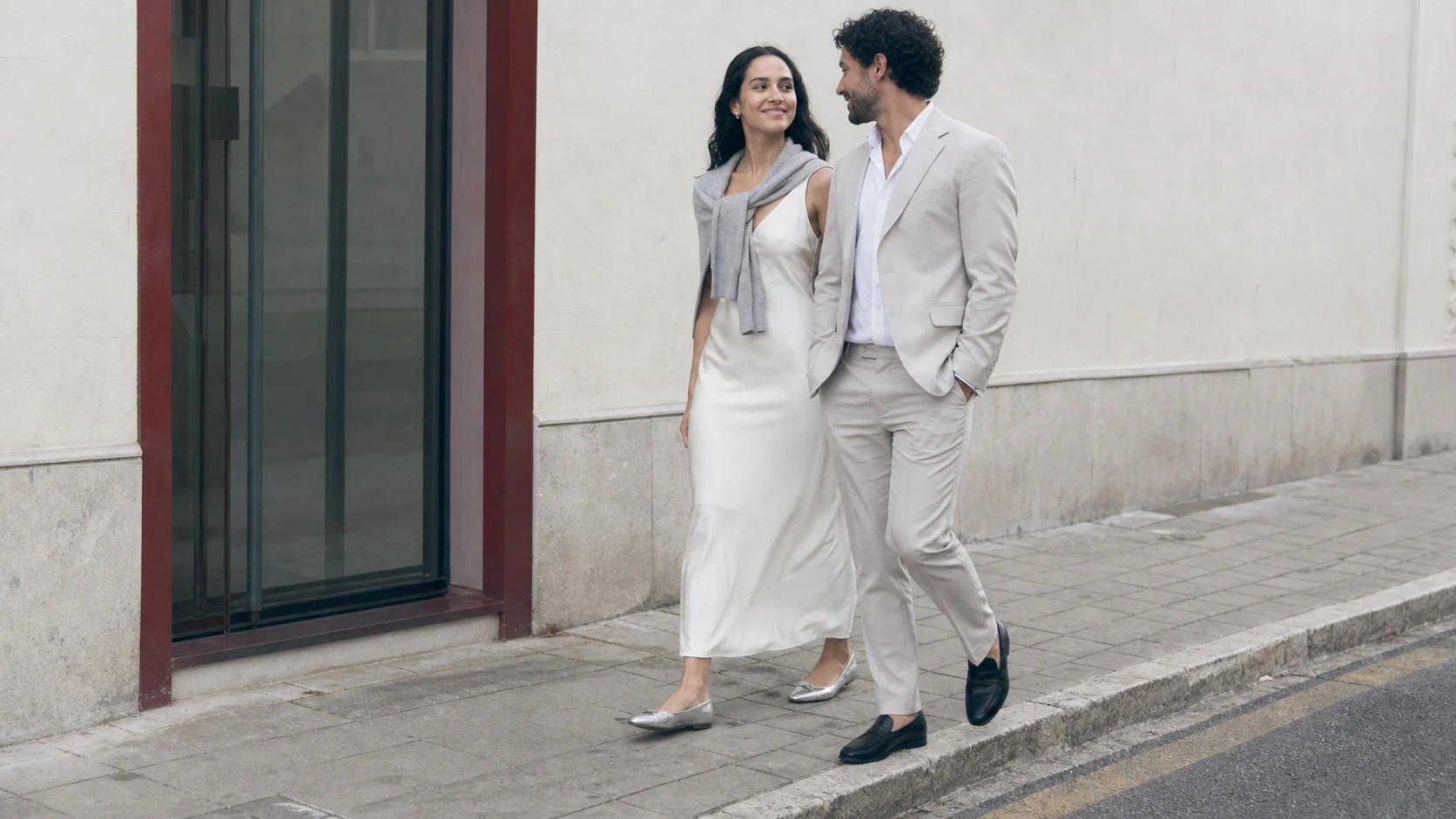 Pareja joven caminando junta antes de su boda en una escena urbana de tonos neutros