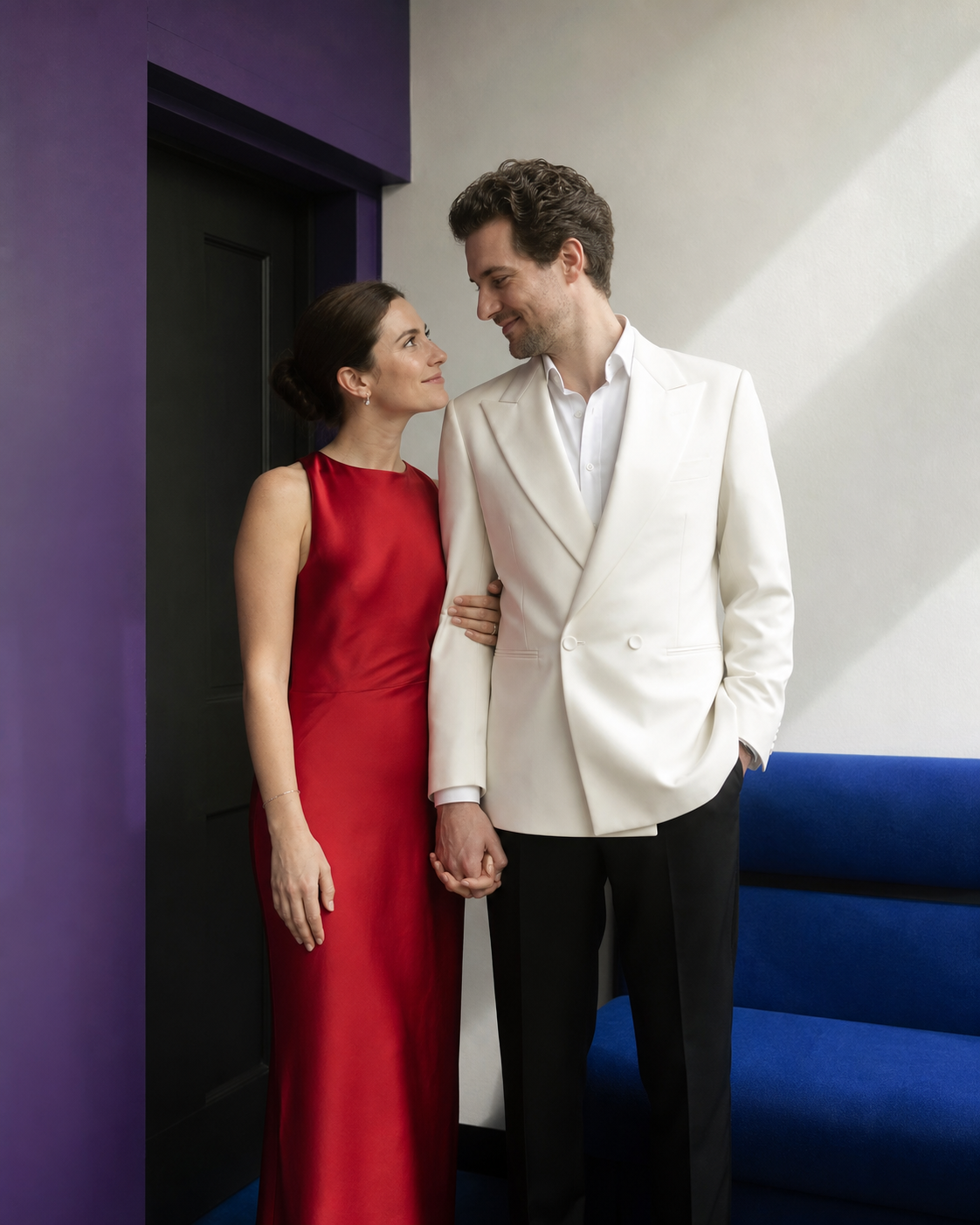 Pareja tomada de la mano se mira en un interior con acentos violeta, rojo y azul