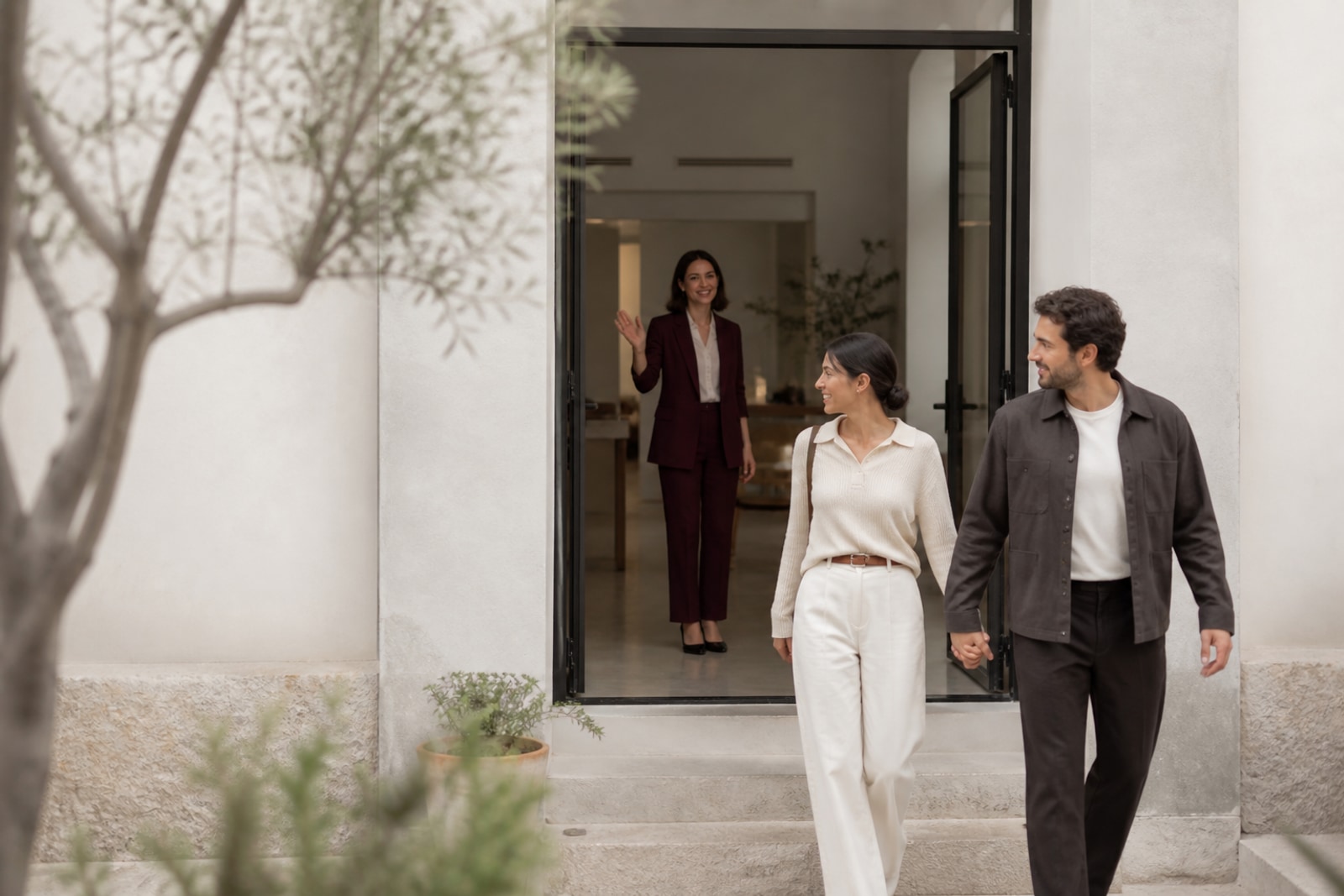 Una pareja sale tomada de la mano mientras su wedding planner se despide desde la puerta.