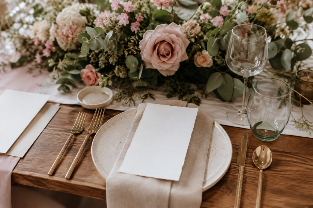 Detalle de mesa de boda con flores rosadas, vajilla artesanal, lino y tarjetas blancas sin texto.